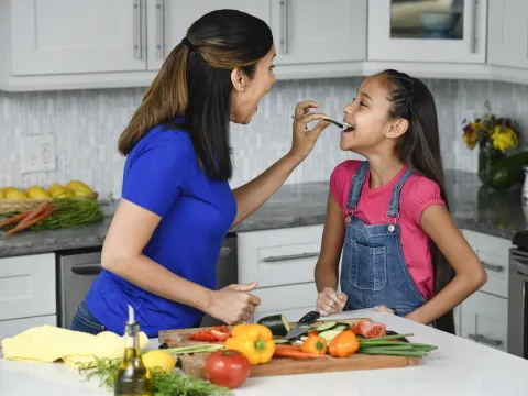 A mother and daughter snacking on vegetables.