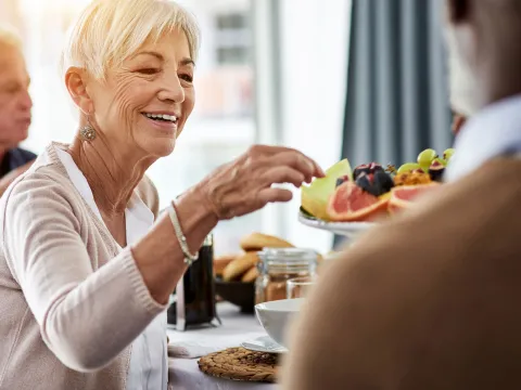 A senior woman picking fruit off from a fruit plate
