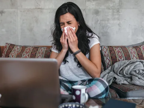 A woman sneezes into a tissue at home