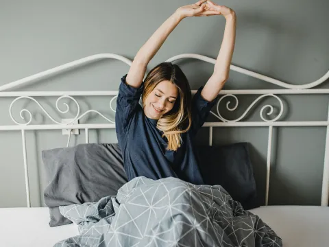 A woman stretching in bed after a good night's sleep.