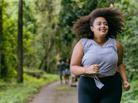 Hispanic woman running outdoors in a forest.