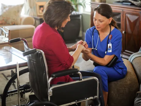 Woman in a wheelchair praying with a home care nurse.