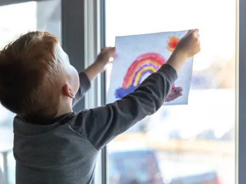 A child holding up a rainbow drawing.