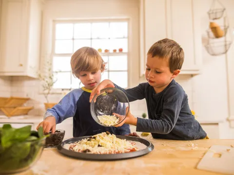 A boy making a veggie pizza with his brother.