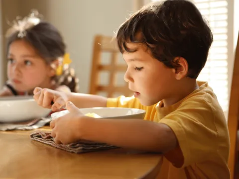 A young boy and girl eating together while at a dining room table together.