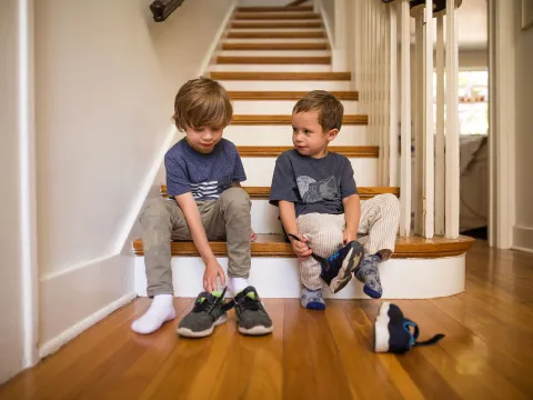 Two brothers getting ready to go out while putting their shoes on.