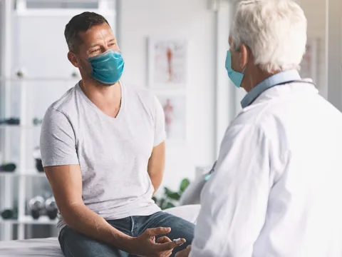 Man talking with doctor while both are wearing masks.