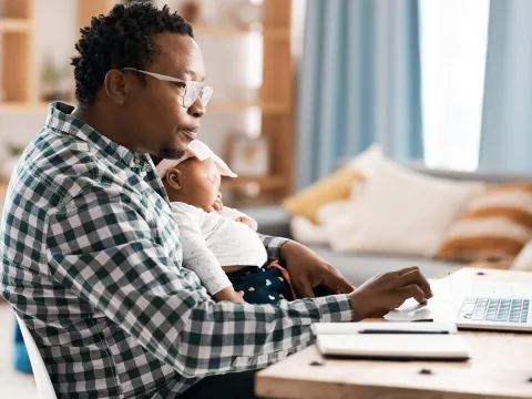 A father working on his computer with his infant on his lap.