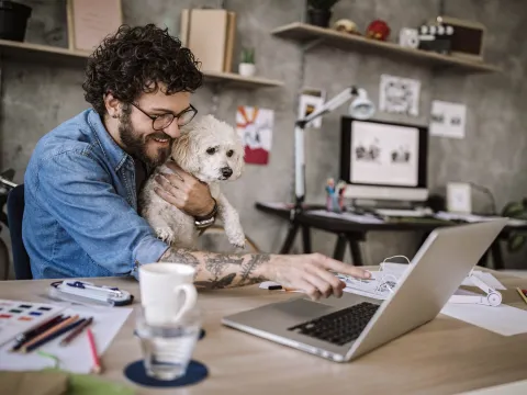 A man working on his laptop with his dog in his lap.