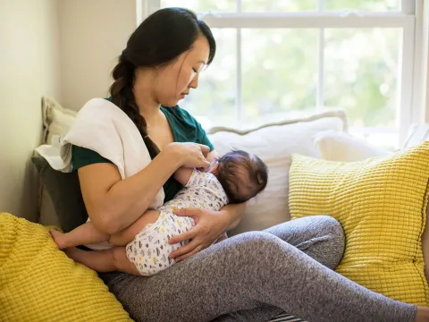 A mother breast-feeding her baby in the couch.
