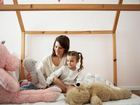 Mother and daughter on a bed with stuffed animals.