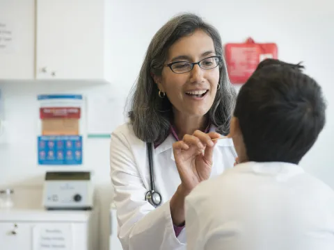 A female doctor looks into a young patient's mouth in an exam room.