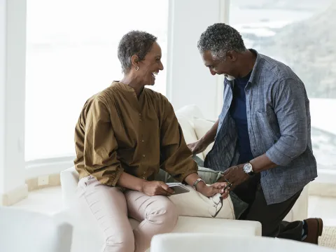 An African American couple smile and laugh on a couch in their home.