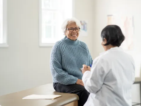 An older female patient talking to a female physician in an exam room.