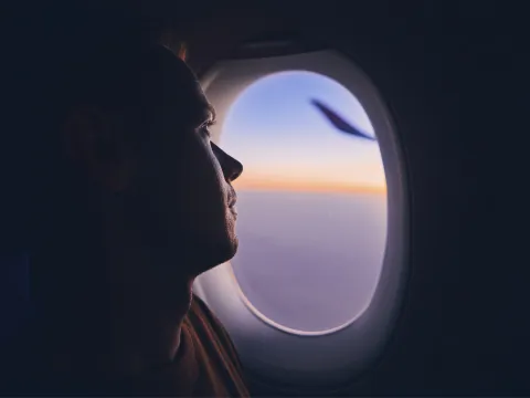 A man looks out the window of a plane during sunset.