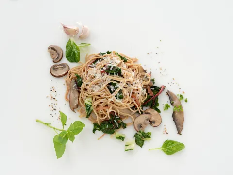 a serving of whole wheat angel hair pasta mixed with greens and mushrooms