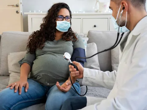 A pregnant woman has a check up while wearing a mask.