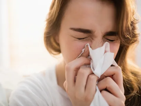 A sick woman blowing her nose into a tissue.