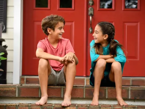 A boy and girl make jokes while sitting on their porch