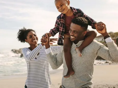 Mother and father walking on beach with son on father's shoulders