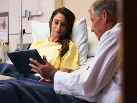 A male doctor goes over a female patient's results on a tablet in her hospital room.