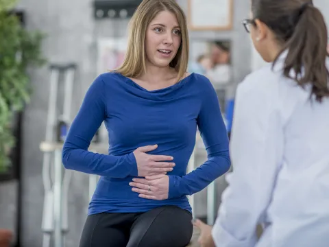 Woman with a stomach ache describes her symptoms to her doctor.