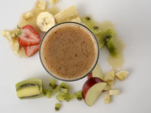 blended fruit in a glass, surrounded by slices of strawberry, banana, kiwi and red delicious apple