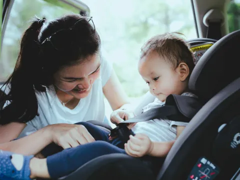 A mother buckles her child into a car seat in the back of a car.