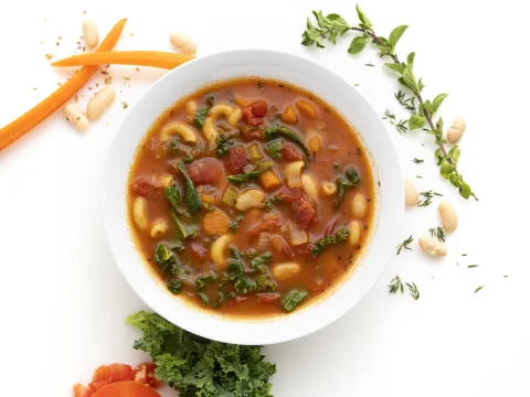 Bowl of white bean and kale soup with carrot and herb garnishes