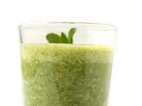Clear glass of green smoothie with sprig on top
