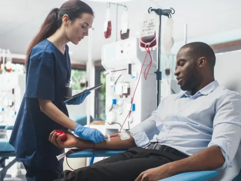 A man sitting in a chair donating blood with the help of a nurse.