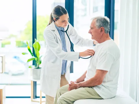 A female physician examining an older man's breathing with a stethoscope.
