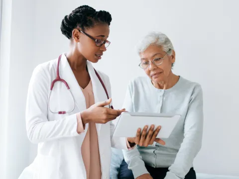 An older female patient and her physician look at a chart.