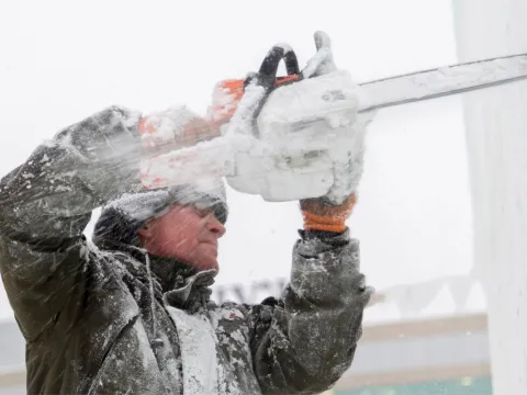 A man using a chainsaw to cut ice.
