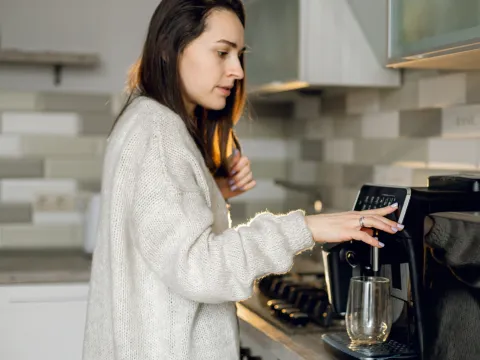 A woman in a kitchen using a coffee machine.