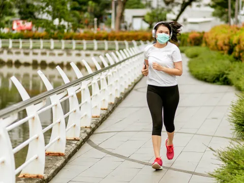 A woman exercising outside with a mask on.