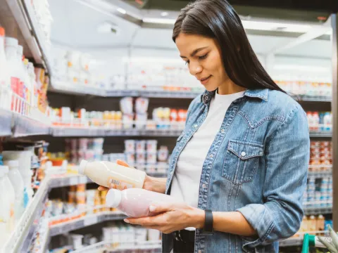 A woman in the dairy aisle of a grocery store holding and looking at bottles.
