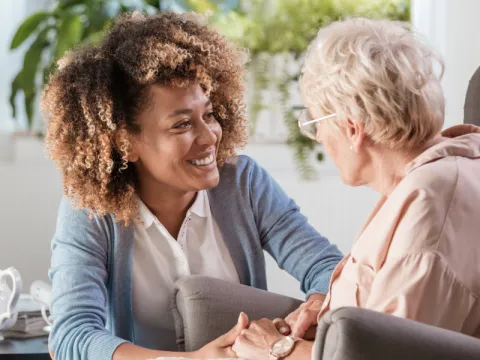 Woman smiling and holding hands with an elderly woman. 