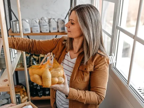 A woman holding a sack of potatoes and a can in a pantry.