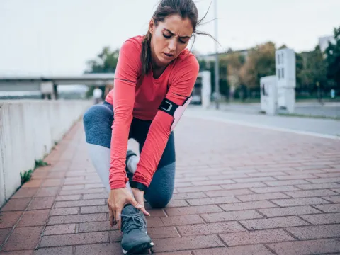 A woman runner holding her ankle while outdoors.