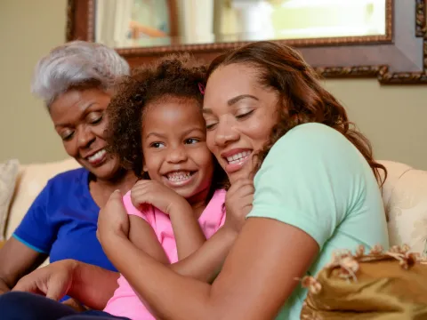 A mother, daughter, and grandmother hug each other on the couch.