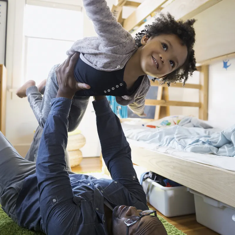 An African American father plays airplane with his daughter.