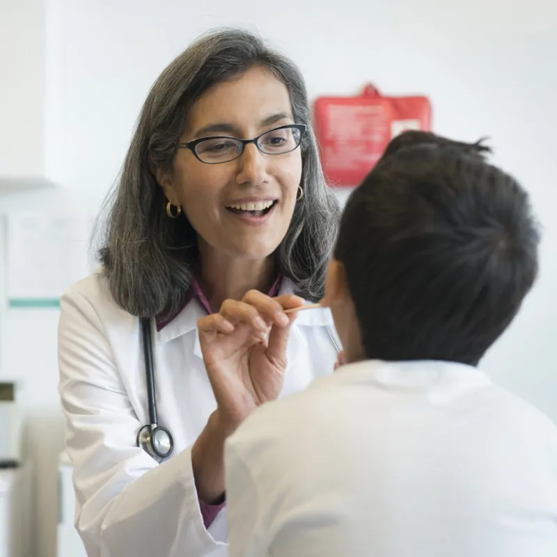 A female doctor looks into a young patient's mouth in an exam room.