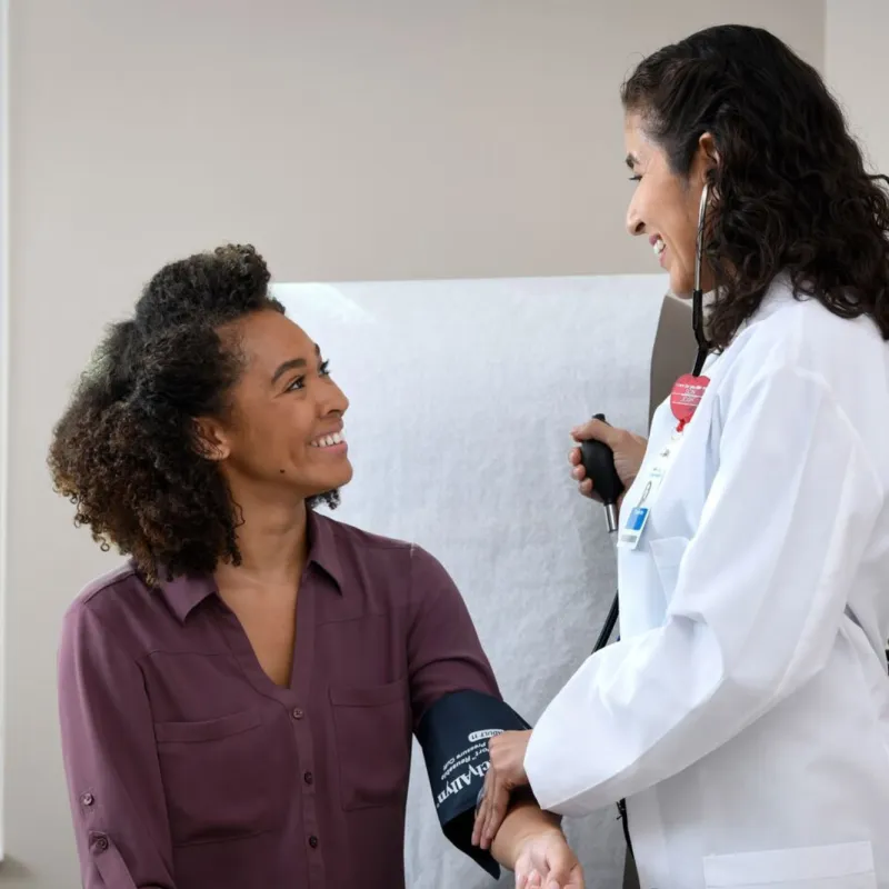 A young woman smiles at her doctor while getting her blood pressure measured.