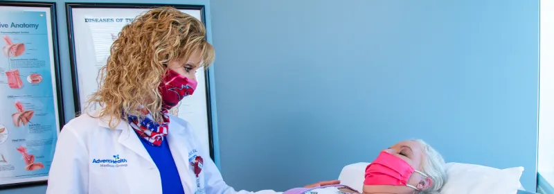 Sharona Ross examing a patient laying on an examination table while both are wearing masks.