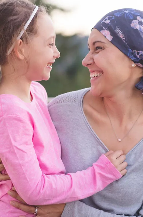A mother and cancer survivor is sitting, with one arm around her daughter.