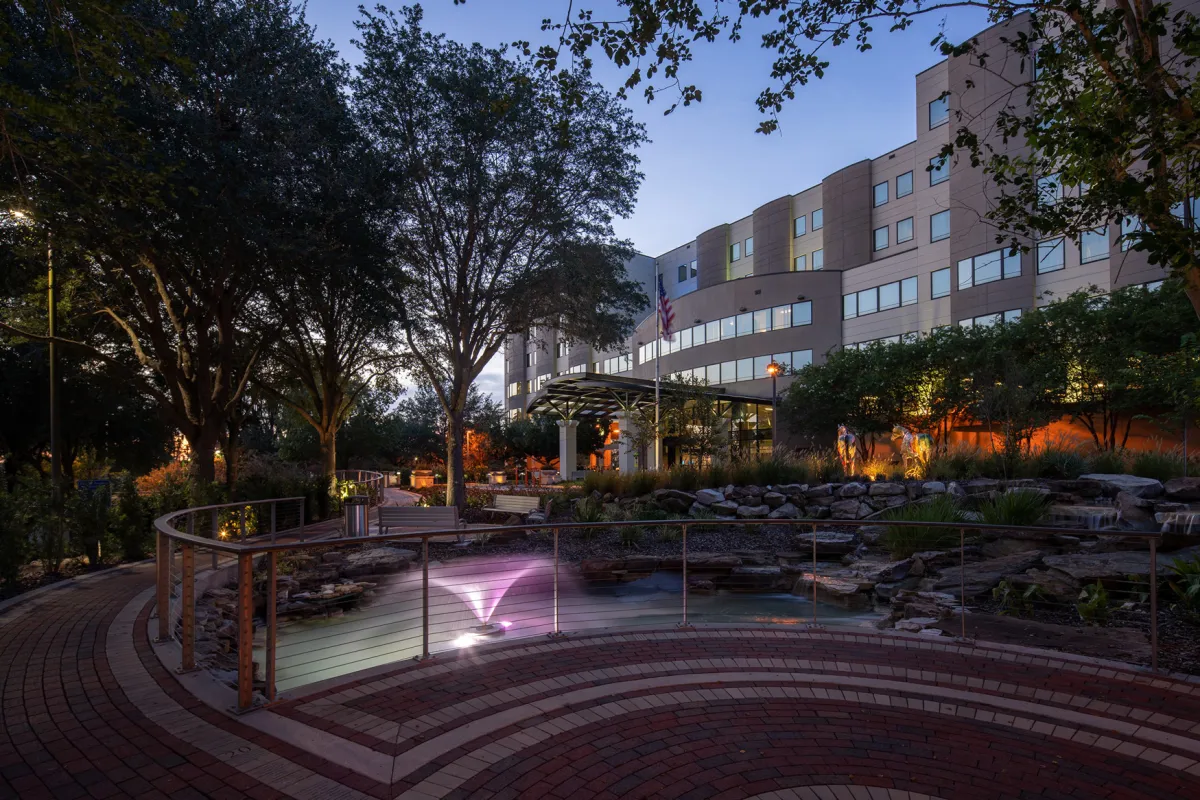 A photo of AdventHealth Ocala taken at dusk. A brick walking path with a railing is in the foreground and the hospital is in the background.