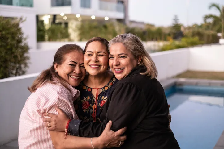 Female Latin friends hugging each other and laughing at home