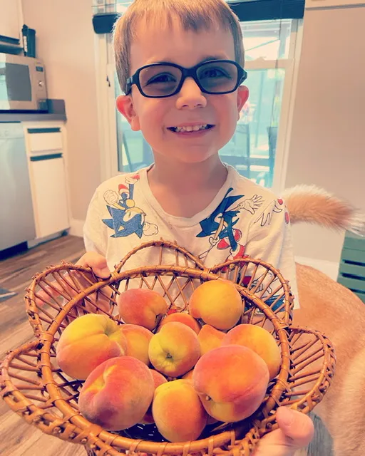 Stephanie Thieman's son presenting harvested peaches from their garden.